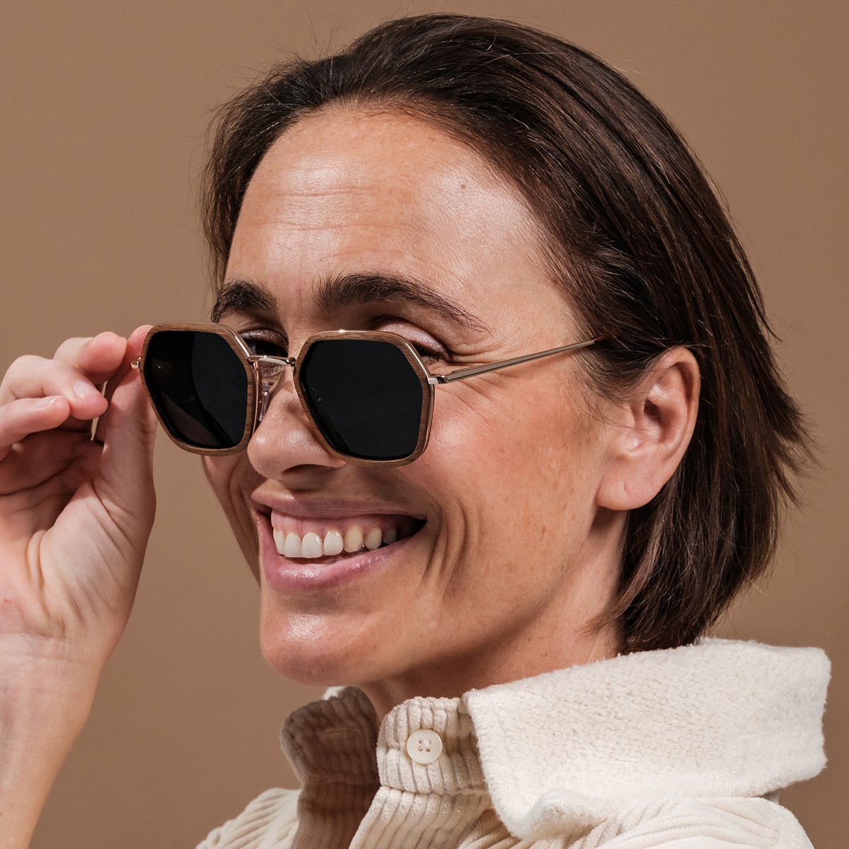 "The Sincere" sunglasses featuring a walnut frame and matte gold accents, worn by a smiling woman.
