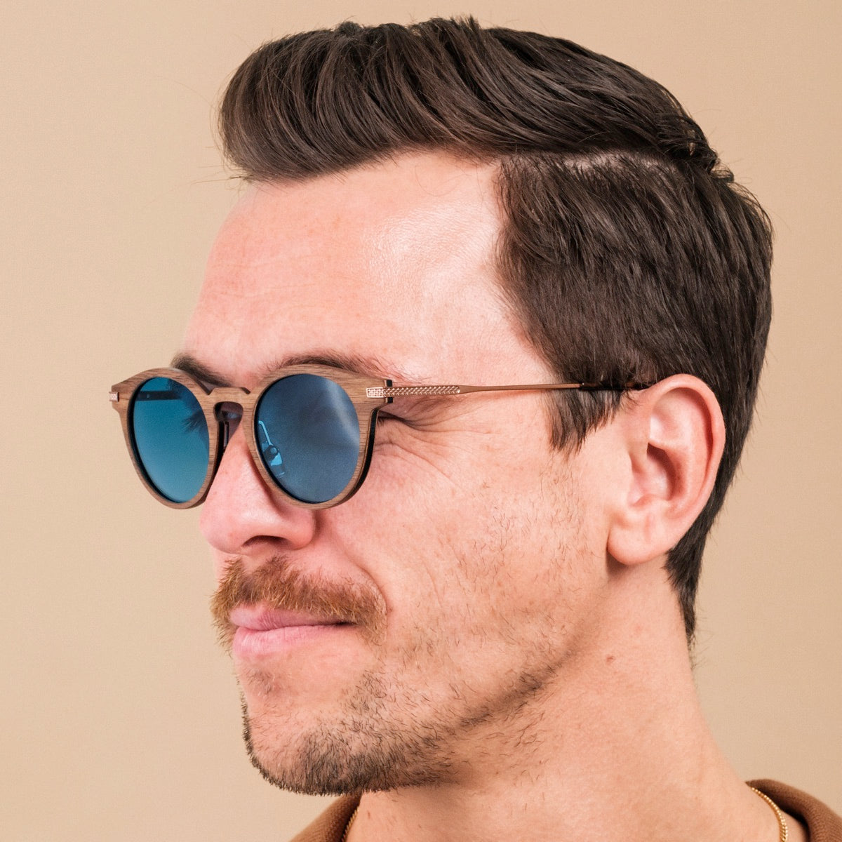 "The Maverick" sunglasses featuring a walnut frame and bronze accents with blue lenses.