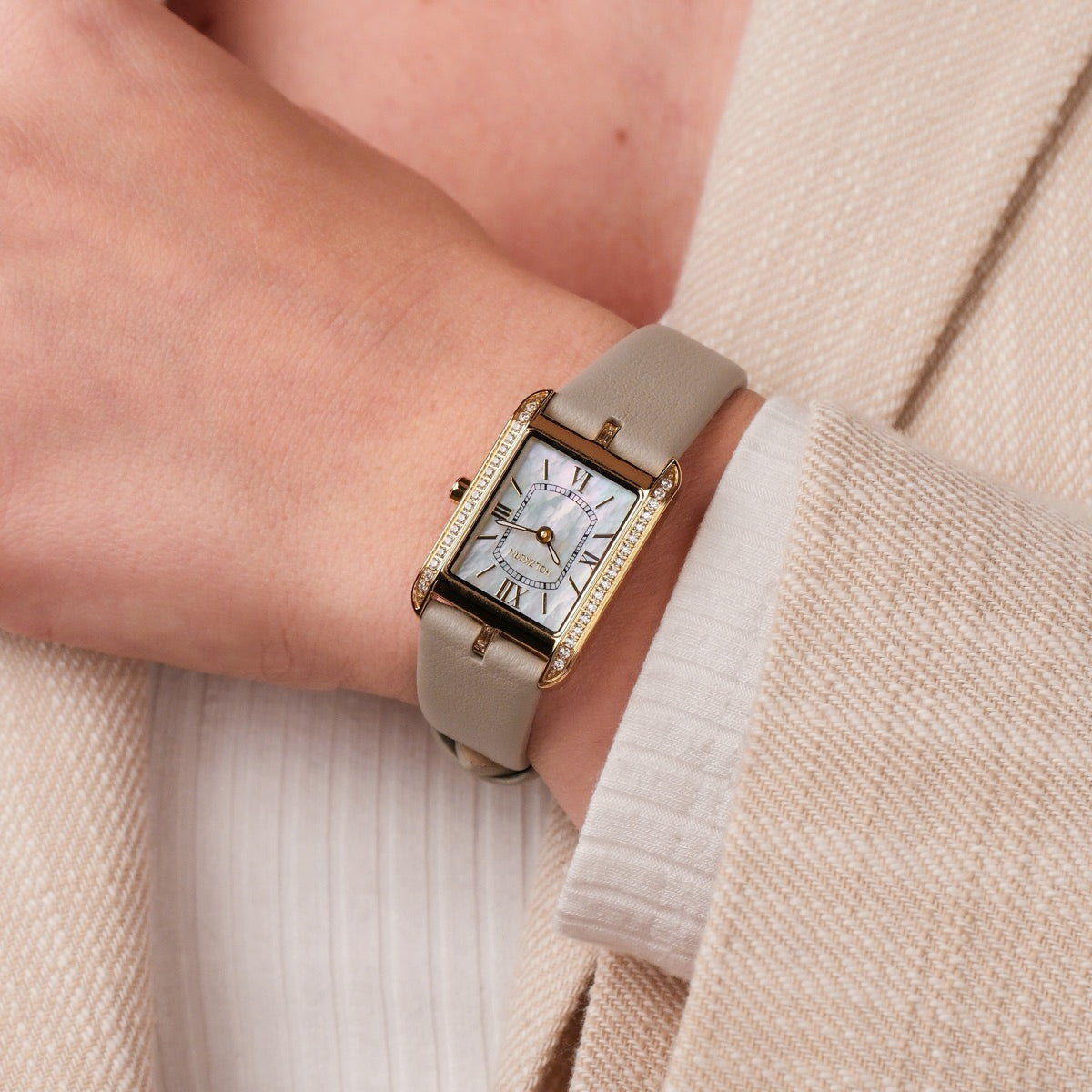 "Memoire" watch featuring a nacre face, gray leather strap, and elegant gold-toned rectangular case.