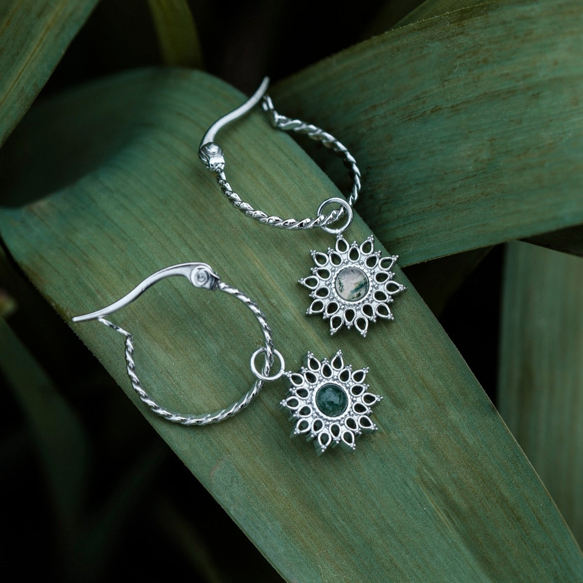 "Suncatcher Earrings" earrings, sunburst style with marble and silver, elegantly arranged on greenery.