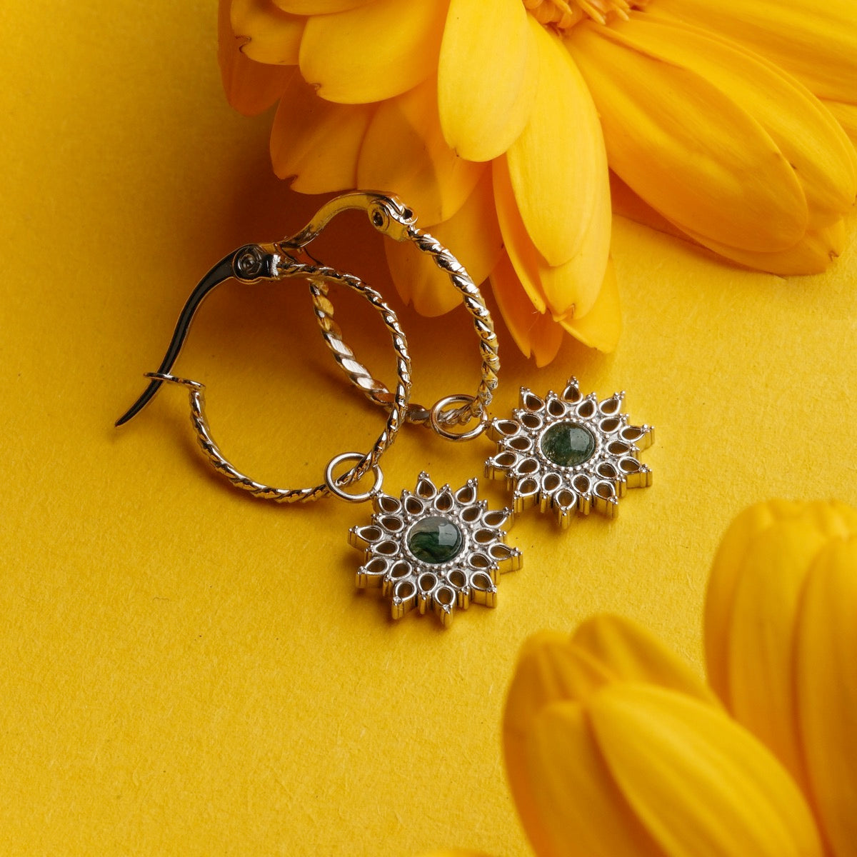 "Suncatcher Earrings", elegant earrings with a marble and silver design, surrounded by vibrant yellow flowers.