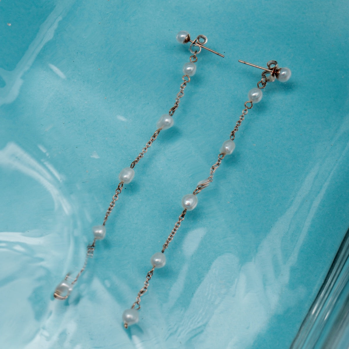 "Summersweet Earrings II" earrings, elegant pearl and rose gold design against a turquoise background.