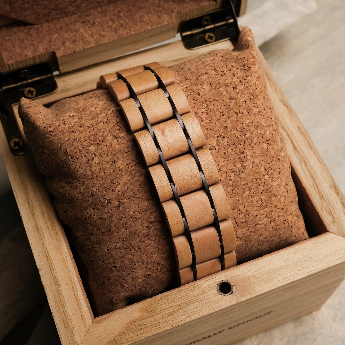 "Grandezza" reloj con un arce y diseño púrpura oscuro, elegantemente mostrado en un cojín de corcho dentro de una caja de madera.