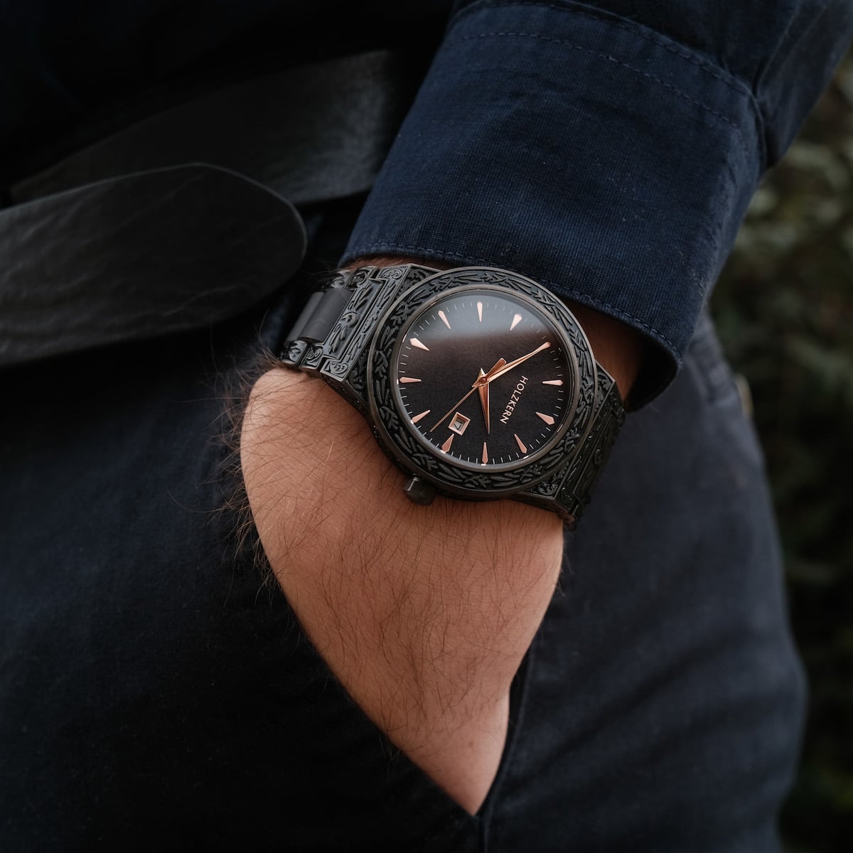"Khalili" reloj con un diseño elegante y todo negro y detalles intrincados, usado con un traje casual.