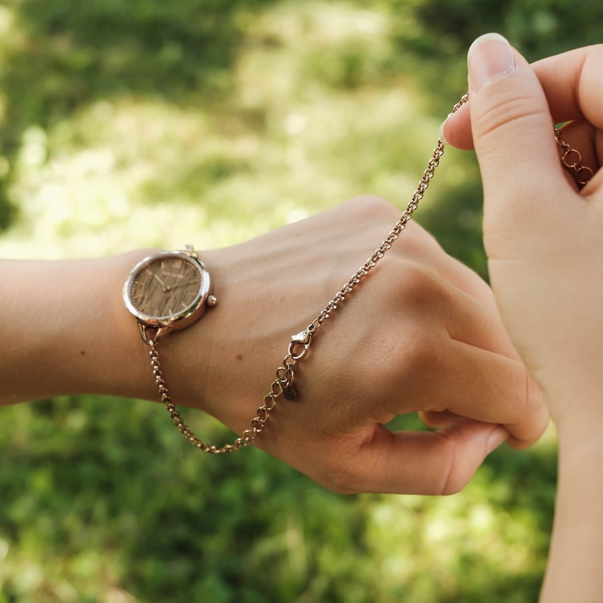 Bracelet fastening tool, a bracelet fastening tool in rose gold, shown in use outdoors.