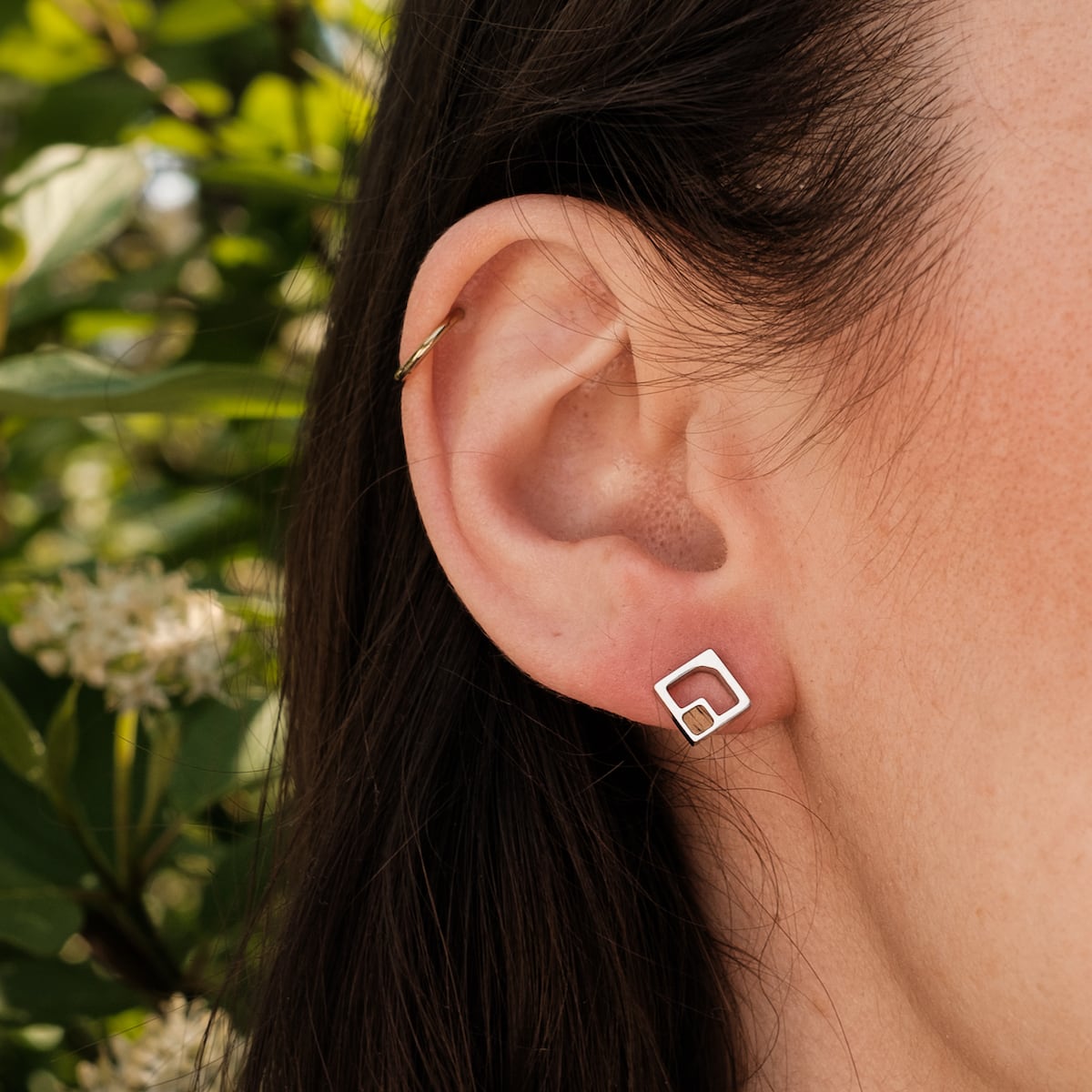 "Geometric Earrings" earrings featuring a geometric silver design with koa wood accents, worn on an ear.