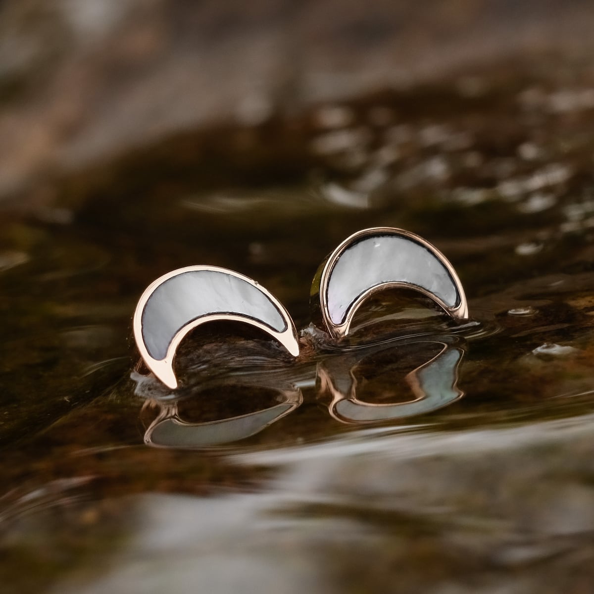 "Hue Earrings" earrings, featuring a crescent design in white nacre and rose gold, elegantly reflected on a watery surface.