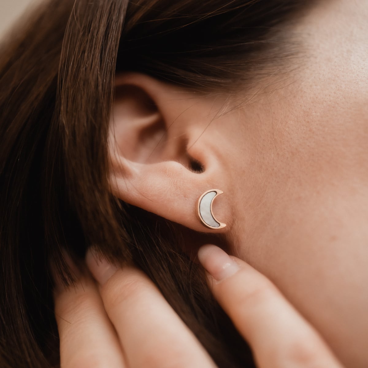 "Hue Earrings", crescent-shaped earrings with white nacre and rose gold accents, worn on an ear.