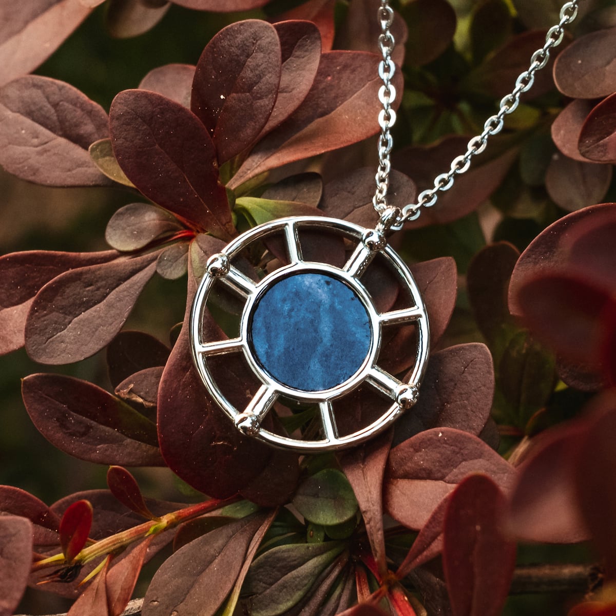 "Amulet Necklace", an elegant marble and silver amulet necklace, showcased against a backdrop of dark foliage.