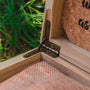 Boîte en bois avec charnières rustiques et détails en liège, placée sur un fond extérieur naturel.